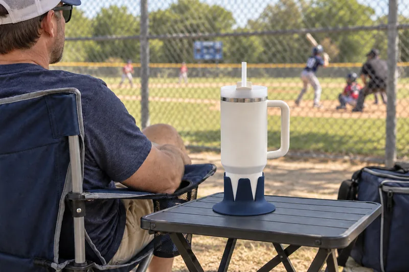 A water tumbler in Navy Steadi on a side table outside a baseball fence. AI lifestyle illustration.